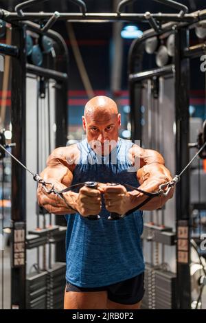 Bodybuilder bald fare esercizio al petto sulla macchina trasversale in palestra Foto Stock