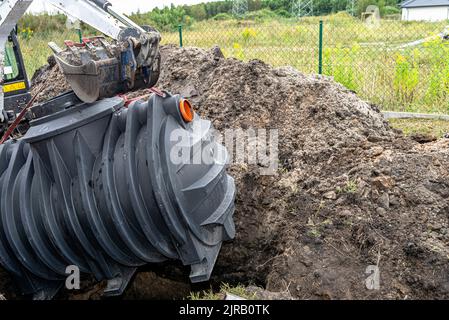 Installazione di un impianto di trattamento delle acque reflue domestiche a camera singola, l'escavatore solleva il serbatoio. Foto Stock