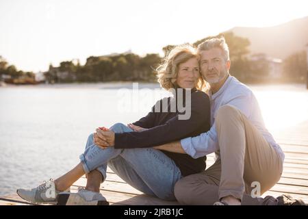 Felice coppia matura seduta sul molo durante la giornata di sole Foto Stock