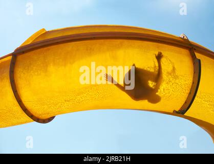 Silhouette di persona che scivola giù scivolo d'acqua Foto Stock