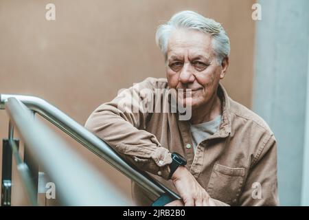 Un uomo anziano sorridente che si appoggia alla ringhiera Foto Stock