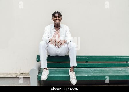 Felice giovane uomo seduto davanti al muro Foto Stock