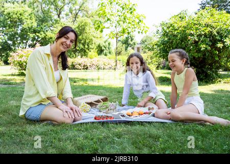 Madre felice con le figlie che hanno picnic al parco Foto Stock