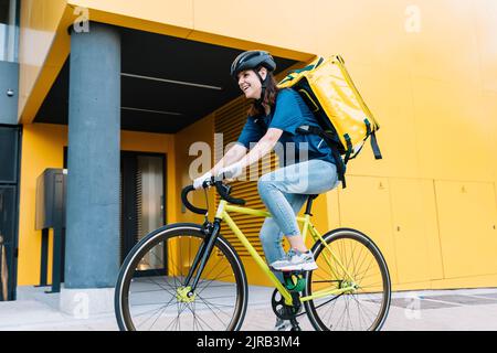 Felice donna consegna in bicicletta di fronte all'edificio Foto Stock