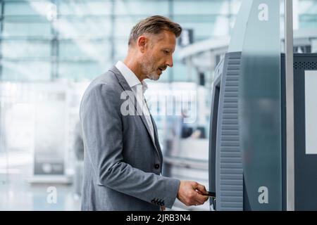 Uomo d'affari maturo che inserisce la carta di credito in bancomat Foto Stock