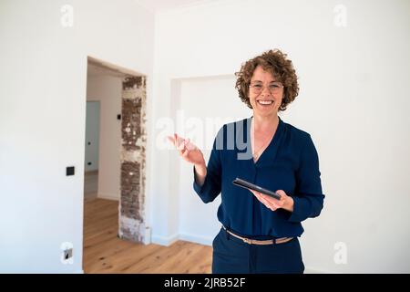 Sorridente agente immobiliare indossando occhiali che tengono il tablet PC a casa Foto Stock