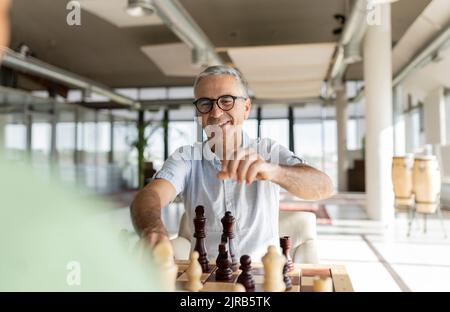 Uomo d'affari maturo felice che gioca a scacchi con un collega in ufficio Foto Stock