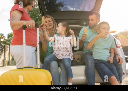 Famiglia felice che mangia i ghiaccioli seduti sul retro dell'auto Foto Stock