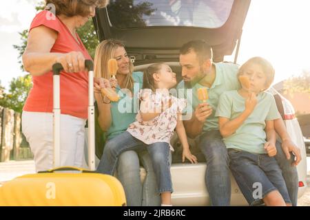 Famiglia sorridente che mangia i ghiaccioli seduti nel bagagliaio dell'auto Foto Stock