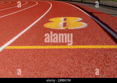 Primo piano sulla corsia numero 8 su una nuova pista rossa con linee di corsia bianche e altre marcature. Foto Stock