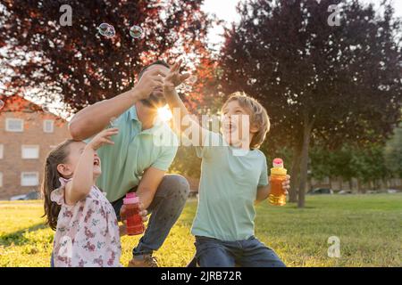 Uomo che soffia bolle da figlio e figlia al parco Foto Stock