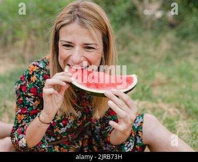 Donna sorridente che mangia anguria al parco Foto Stock