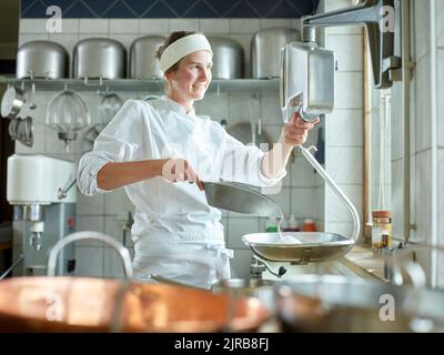 Buon giovane pasticciere che misura lo zucchero su scala in cucina Foto Stock