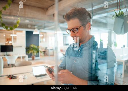 Messaggi di testo maturi per gli uomini d'affari tramite smartphone visti attraverso il vetro in ufficio Foto Stock
