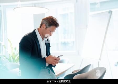 Messaggi di testo maturi per gli uomini d'affari tramite telefono cellulare in ufficio Foto Stock