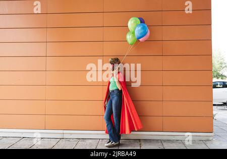 Donna che indossa maschera di coccodrillo appoggiata con palloncini multicolore sulla parete Foto Stock