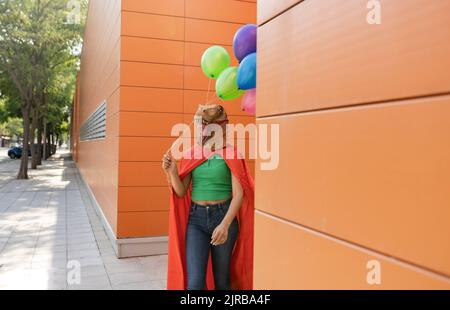 Donna che indossa una maschera di coccodrillo camminare con palloncini multicolore davanti al muro Foto Stock