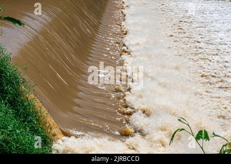 Rapide di acqua fangosa in rapido movimento su uno stramazzo e cadere giù spruzzi, schiumando su un fiume. Foto Stock