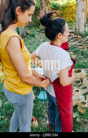 Donna aiutare l'amico a indossare grembiule in giardino Foto Stock