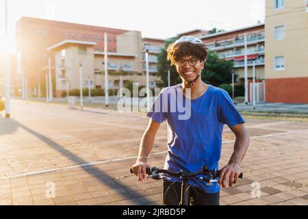 Felice uomo che indossa il casco in piedi con la bicicletta in città Foto Stock