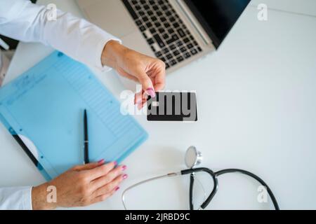 Medico che tiene la scheda sopra la scrivania in pratica medica Foto Stock