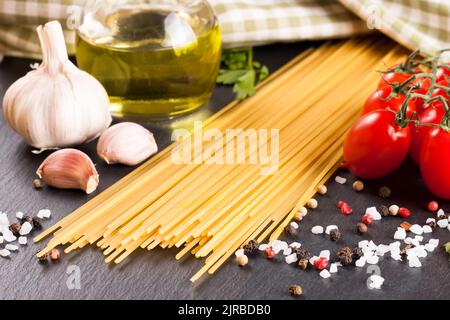 Pasta e ingridienti di cottura su superficie di ardesia nera. Spaghetti, pomodoro, olio d'oliva, aglio, prezzemolo e spezie. Cucina italiana Foto Stock