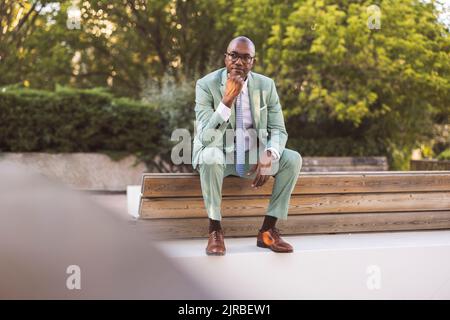 Uomo d'affari maturo e premuroso seduto su una panca nel parco Foto Stock