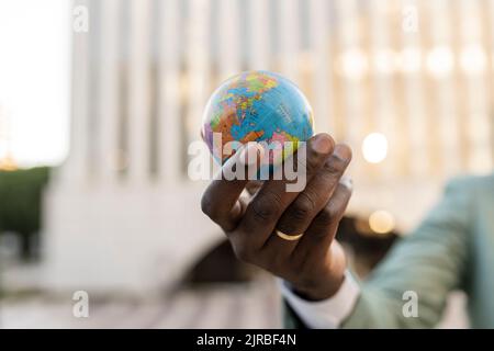 Mano di uomo d'affari maturo che tiene figurina del globo Foto Stock