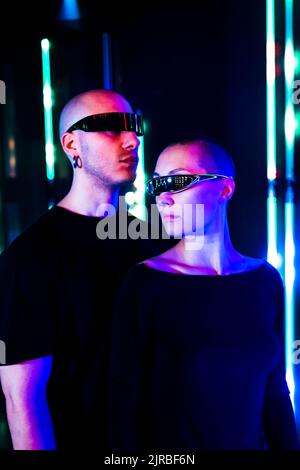 Uomo e donna che indossano occhiali intelligenti davanti all'illuminazione al neon Foto Stock