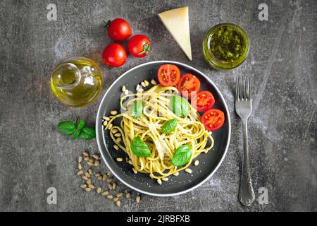Pasta tradizionale italiana con verdure fresche, parmigiano, foglie di basilico, pinoli e salsa al pesto in ciotola nera su fondo di pietra grigia. In alto Foto Stock