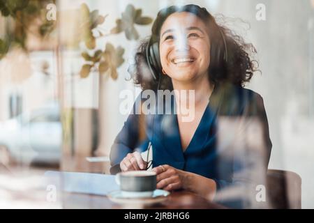 Donna allegra che indossa cuffie e ascolta la musica nel bar Foto Stock
