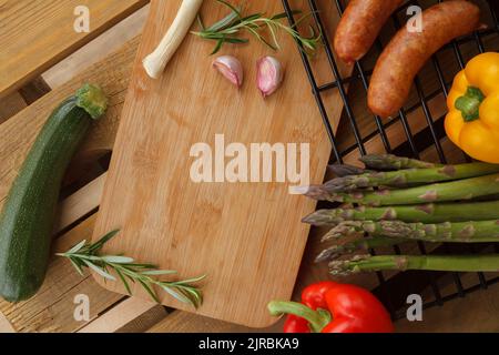 Verdure e salsicce preparate per la cottura alla griglia. Composizione di posa piatta con spazio copia su tavola da cucina in legno. Foto Stock