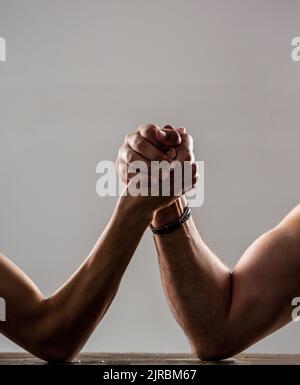 Le mani di due uomini hanno stretto un braccio di lotta, forte e debole, partita iniqua. Braccio uomo pesantemente muscoloso che lotta contro un uomo debole puny Foto Stock