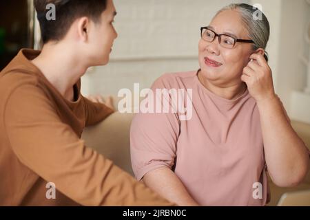Felice donna anziana mettere in auricolari nipote ha presentato per il compleanno Foto Stock