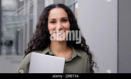 Felice adulto 30s caucasico donna ispanica professionale business project manager imprenditore donna imprenditore tenendo notebook guardando la fotocamera sorridente Foto Stock