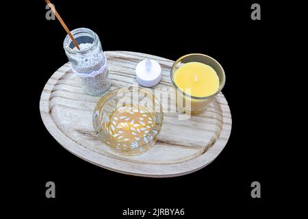 Semplice centrotavola decorativa su uno sfondo nero studio, posacenere di vetro con foglie bianche, candela gialla in un supporto, incenso in un vaso con whi Foto Stock