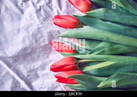 Primo piano di bellissimi tulipani rossi su carta stropicciata. Composizione primaverile. Delicato bouquet di tulipani rossi, vista dall'alto. Con spazio per copiare. Foto di alta qualità Foto Stock