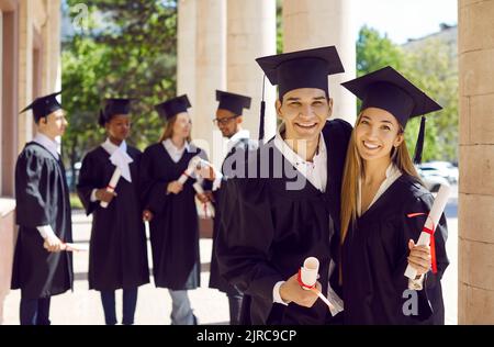 Ritratto di amici felici con diplomi che abbracciano e sorridono il giorno della laurea Foto Stock
