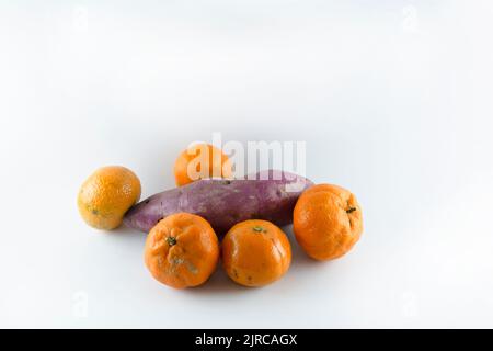 Superficie coperta con cinque tangerini freschi maturi e una patata dolce. Composizione isolata su sfondo bianco. Foto Stock