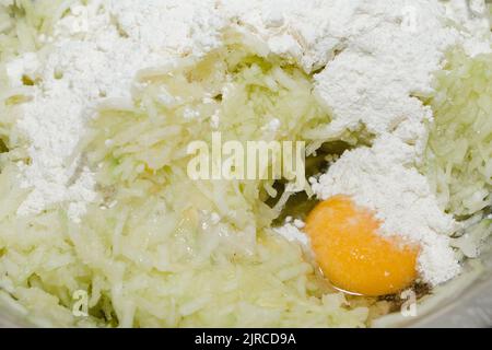 Ricetta per le frittelle di zucchine. Passaggio 3 - miscelazione dell'impasto per frittelle vegetali. Farina, uovo e zucchine verdi. Foto Stock