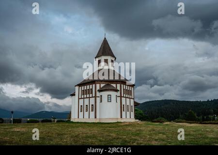 Piccola cappella bianca rurale Tesarovska con cimitero nel villaggio di Korenov, Jizera montagne, Repubblica Ceca. Paesaggio estivo, stormy Sky.Wooden histori Foto Stock