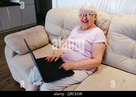 donna anziana felice che usa un computer portatile a casa. Donna anziana anziana matura che guarda corsi di formazione aziendale, webinar online sul lavoro remoto dei computer portatili Foto Stock