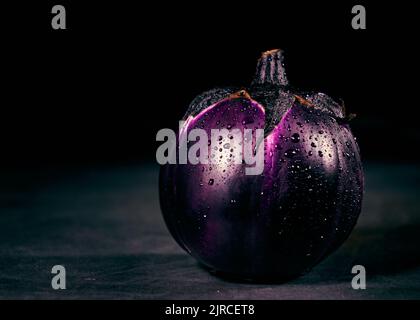 Una melanzana rotonda con gocce d'acqua su fondo scuro Foto Stock