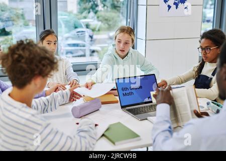 Vista ad angolo alto a diversi bambini in attività di gruppo in classe scolastica, concentrarsi sulla ragazza teen che consegna carte al compagno di classe Foto Stock