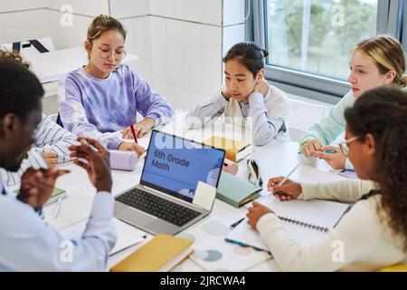 Vista ad alto angolo di diversi bambini in attività di gruppo in classe scolastica, focalizzazione sul giovane asiatico che parla Foto Stock