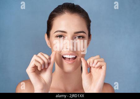 Prendendosi cura dei suoi bianchi perlacei. Studio ritratto di una giovane donna attraente che le gallina i denti su uno sfondo grigio. Foto Stock