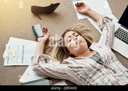 Ci sono solo troppe richieste da tenere il passo. Colpo ad angolo alto di una donna d'affari stressata sdraiata sul pavimento in un ufficio. Foto Stock