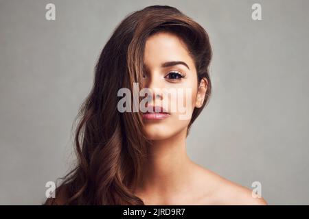 La bellezza sta fluendo i capelli e la pelle incandescente. Studio shot di una giovane bella donna con lunghi capelli gorgeous che posano su uno sfondo grigio. Foto Stock