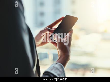 Tenersi in contatto. Una giovane donna d'affari irriconoscibile che usa il suo cellulare in ufficio. Foto Stock