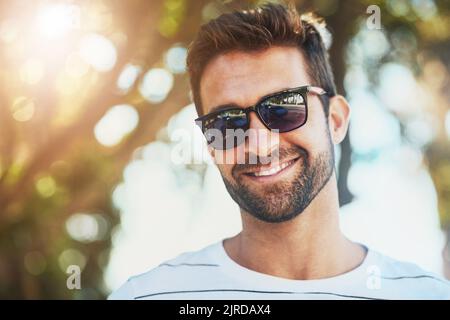 Mantenere il suo sguardo fresco per quei giorni caldi. Ritratto corto di un bel giovane uomo che indossa occhiali da sole in una giornata estiva all'aperto. Foto Stock